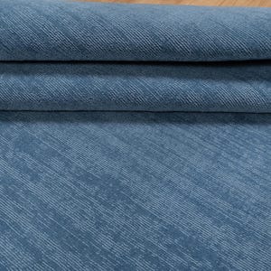 May include: Close-up of a folded blue fabric with a textured, diagonal striped pattern. The fabric has a soft, slightly faded appearance. The material is likely used for upholstery or home decor.