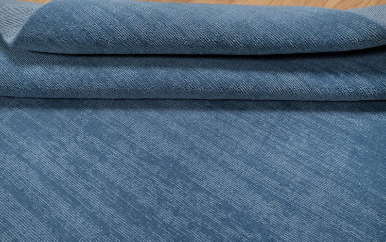 May include: Close-up of a folded blue fabric with a textured, diagonal striped pattern. The fabric has a soft, slightly faded appearance. The material is likely used for upholstery or home decor.