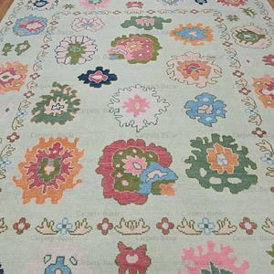 May include: A light green rug with a floral pattern. The rug features a variety of colors, including pink, blue, green, and orange. The flowers are arranged in a symmetrical pattern.