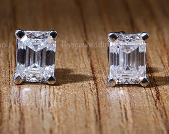 Könnte beinhalten: Zwei quadratisch geschliffene Diamant-Ohrstecker mit Silberfassung. Die Diamanten sind klar und funkelnd, vor einem warmen, hölzernen Hintergrund. Die Ohrringe sind ein klassisches Schmuckstück.