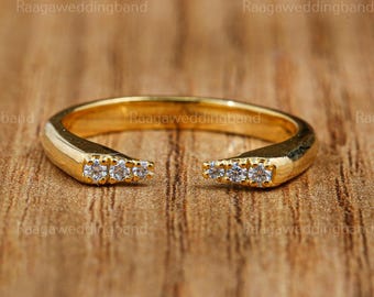 May include: A gold-colored open ring with small, clear gemstones set on each end. The ring has a smooth, polished finish and is set against a warm, wooden background. The ring's design is modern and minimalist, suitable for everyday wear.