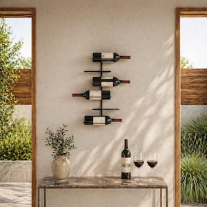 May include: A black metal wall-mounted wine rack holding four bottles of red wine. A bottle of wine and two wine glasses sit on a table below the rack. A vase with greenery is on the table.