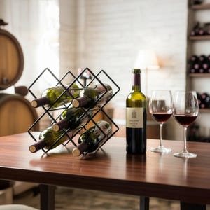 Könnte beinhalten: Ein schwarzes Weinregal aus Metall mit mehreren Weinflaschen. Eine Weinflasche und zwei Weingläser mit Rotwein stehen auf einem Holztisch. Die Weinflasche hat ein Etikett.