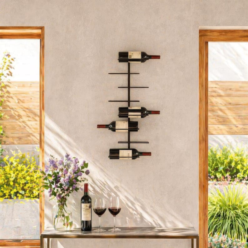 May include: A black metal wall-mounted wine rack holding four bottles of wine. The rack has a minimalist design with horizontal bars to support the bottles. The bottles are displayed against a light gray wall, with a table and wine glasses in the foreground.