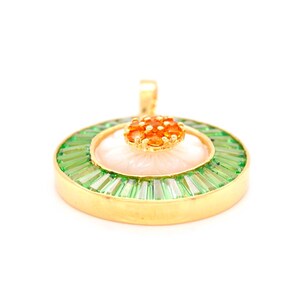 May include: A gold pendant with a floral design. The pendant features a central flower with a pink center and orange gemstone accents. The flower is surrounded by a ring of green baguette-cut gemstones, all set in a gold frame.