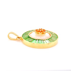 May include: A gold pendant with a floral design. The pendant features a central white flower, surrounded by green baguette-cut stones and a small orange flower on top. The pendant has a gold bail.