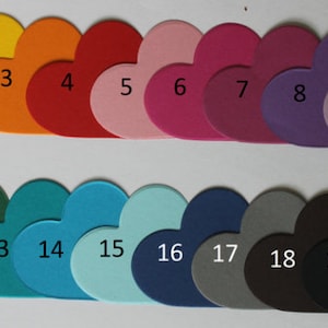 Könnte beinhalten: Eine Farbkarte mit 19 herzförmigen Papiermustern, nummeriert von 1 bis 19. Die Farben reichen von Weiß bis Schwarz, mit Schattierungen von Gelb, Orange, Rot, Rosa, Lila, Grün, Blau und Grau.