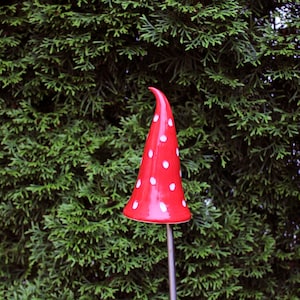 Op de afbeelding: Een rode keramische paddenstoel tuinpaal met witte stippen. De paddenstoelvormige decoratie is gemonteerd op een metalen staaf, perfect om een ​​gril aan elke tuin of buitenruimte toe te voegen.