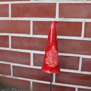 Könnte beinhalten: Ein roter Keramik-Gnomhut mit weißem Blumenmuster. Der Hut sitzt auf einem Metallstab.