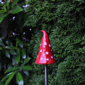 Könnte beinhalten: Ein roter und weißer Keramik-Pilz-Gartenpfahl mit weißen Punkten. Der Pfahl ist aus Metall und wird in den Boden gesteckt.
