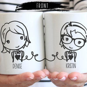 May include: Two white ceramic mugs with black line drawings of women wearing glasses and holding hearts. The mugs are connected by a line and the text "Denise" and "Kristin" is printed below the drawings.