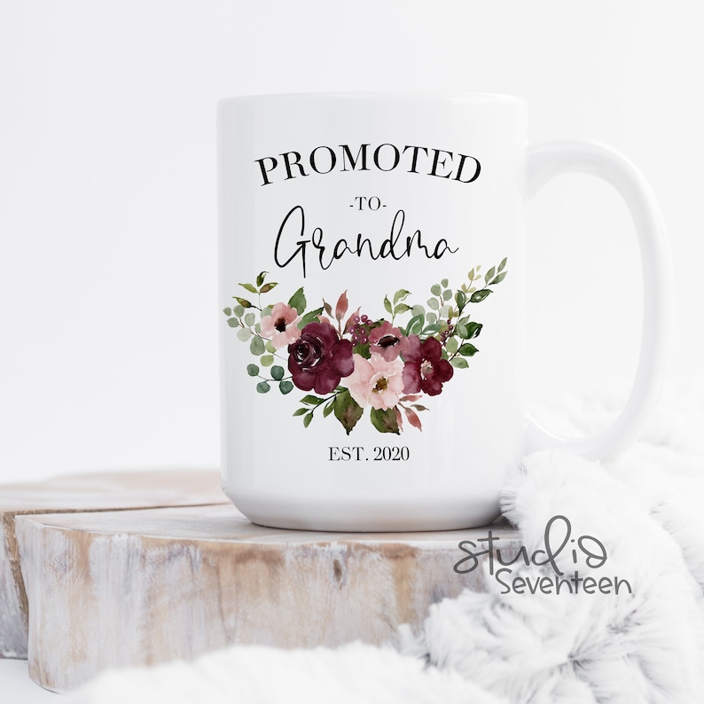 May include: White ceramic mug with the text "Promoted to Grandma Est. 2020" and a floral design in shades of burgundy and pink.