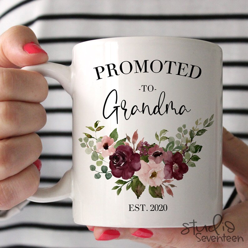 May include: White ceramic mug with the text "Promoted to Grandma Est. 2020" and a floral design in shades of pink and burgundy.