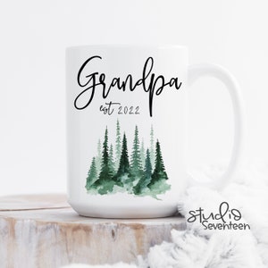 May include: White ceramic mug with a black and white design that says "Grandpa est 2022". The design also features a watercolour illustration of a forest with green trees.