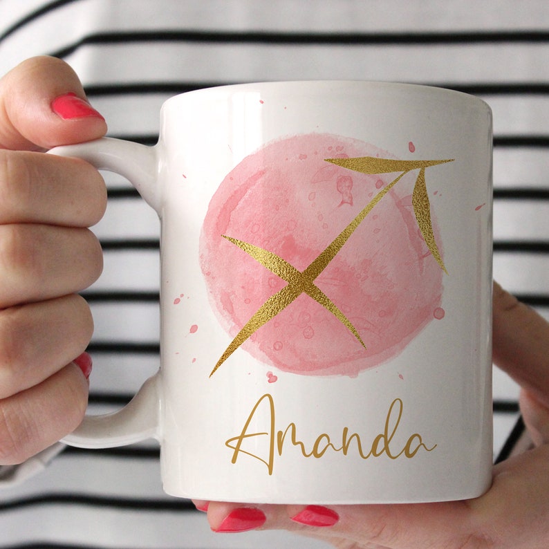May include: White ceramic mug with a pink watercolor circle and gold Sagittarius zodiac symbol. The name "Amanda" is written in gold lettering below the symbol.