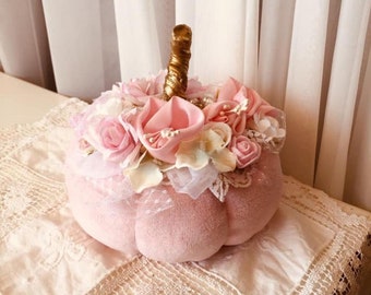 May include: A pink velvet pumpkin with a gold stem, decorated with pink and white flowers and lace.