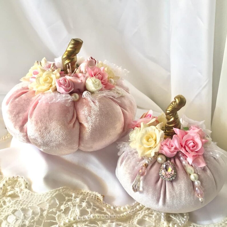May include: Two pink velvet pumpkins decorated with white and pink flowers, gold stems, pearls, and rhinestones.