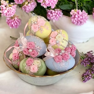 Peut inclure: Un bol d'œufs de Pâques de couleur pastel décorés de dentelle, de rubans et de roses roses. Les œufs sont disposés dans un bol à motif floral bleu clair et blanc.