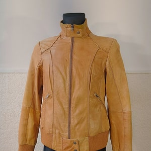 Peut inclure: Une veste en cuir marron avec une fermeture éclair et un col, des poignets et une ceinture en tricot côtelé.