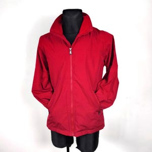 May include: A red zip-up jacket with a stand-up collar and two pockets.