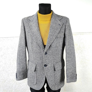 Puede incluir: Una blazer gris con estampado de espiga con dos bolsillos delanteros y dos botones. La blazer se lleva sobre un jersey de cuello alto amarillo. La chaqueta se exhibe en un maniquí negro.