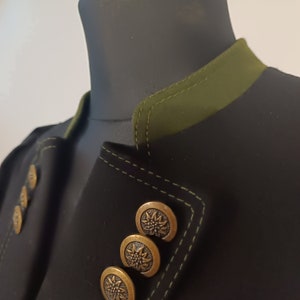 Könnte beinhalten: Eine schwarze Jacke mit grünem Kragen und goldenen Knöpfen. Die Knöpfe haben ein florales Design.