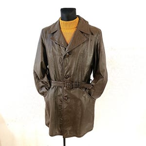 Puede incluir: Una gabardina de cuero marrón con cinturón y cierre de botones. La gabardina tiene cuello y dos bolsillos.