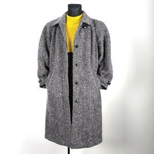 May include: A long, grey and white herringbone patterned coat with a button closure. The coat has a collar and long sleeves.