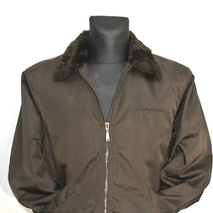 Könnte beinhalten: Eine braune Jacke mit einem Kunstfellkragen und einem Reißverschluss. Die Jacke hat ein Logo auf der Vorderseite.