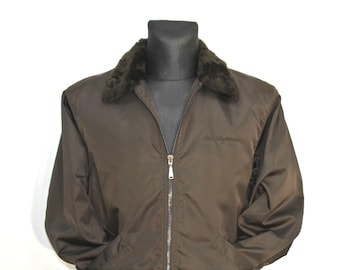 Könnte beinhalten: Eine braune Jacke mit einem Kunstfellkragen und einem Reißverschluss. Die Jacke hat ein Logo auf der Vorderseite.