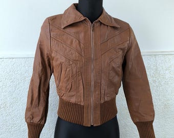 Può includere: Una giacca di pelle marrone con chiusura a zip e fascia in maglia a costine. La giacca ha un colletto e maniche lunghe.