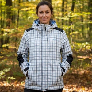 Puede incluir: Chaqueta con capucha a cuadros blancos, azules y negros, con detalles negros en los hombros y las mangas. La chaqueta tiene cierre de cremallera y bolsillos. El fondo es una escena borrosa del bosque.