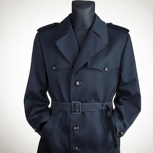 Puede incluir: Un abrigo tipo gabardina azul marino con diseño de doble botonadura. El abrigo tiene cinturón, charreteras y bolsillos abotonados. El abrigo se muestra en un maniquí negro.