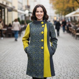 Peut inclure: Une femme porte un long manteau avec un motif géométrique bleu marine, jaune et gris. Le manteau a un col montant, de gros boutons jaunes et des accents jaunes sur les manches et le devant. Le manteau est long jusqu'aux genoux.