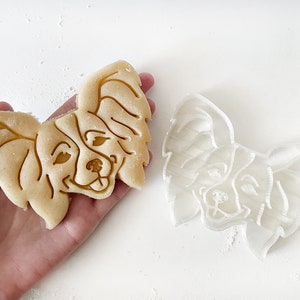 May include: A white plastic cookie cutter and a baked cookie in the shape of a Papillon dog's head.