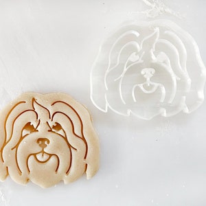 Puede incluir: Dos cortadores de galletas con forma de cabeza de perro. El cortador de la izquierda est&aacute; hecho de masa marr&oacute;n y el cortador de la derecha est&aacute; hecho de pl&aacute;stico transparente.