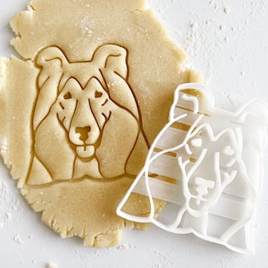 Peut inclure: Un emporte-pièce en plastique blanc en forme de chien Collie. L'emporte-pièce est posé sur une pâte à biscuits qui a été pressée en forme de chien Collie.