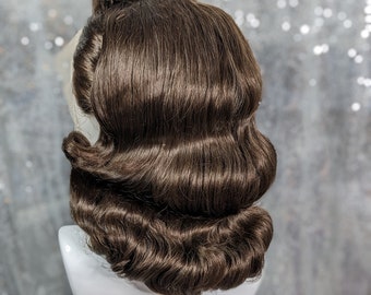 Pode incluir: Uma peruca castanho com um estilo vintage preso com ondas e cachos suaves. A peruca está em uma cabeça de manequim branca.