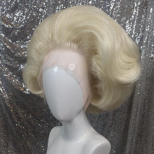 May include: A blonde wig with a bouffant style. The wig is on a white mannequin head.