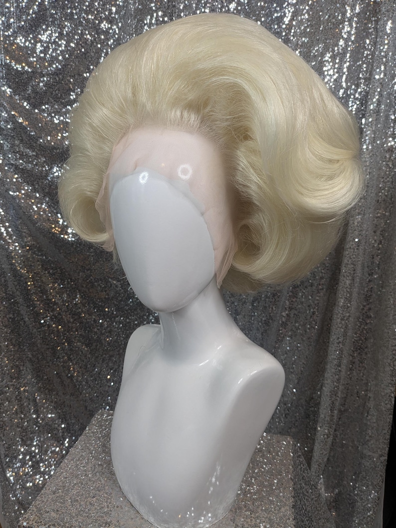 May include: A blonde wig with a bouffant style. The wig is on a white mannequin head.