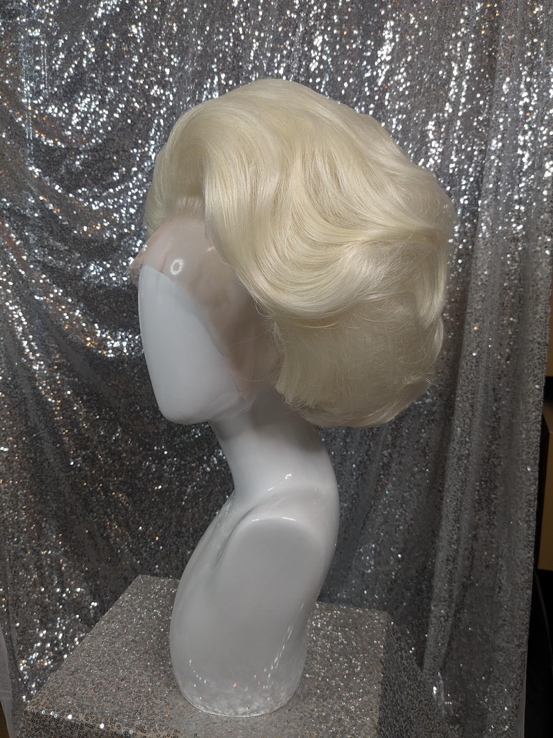 May include: A blonde wig with a side part and a voluminous, wavy style. The wig is on a white mannequin head.