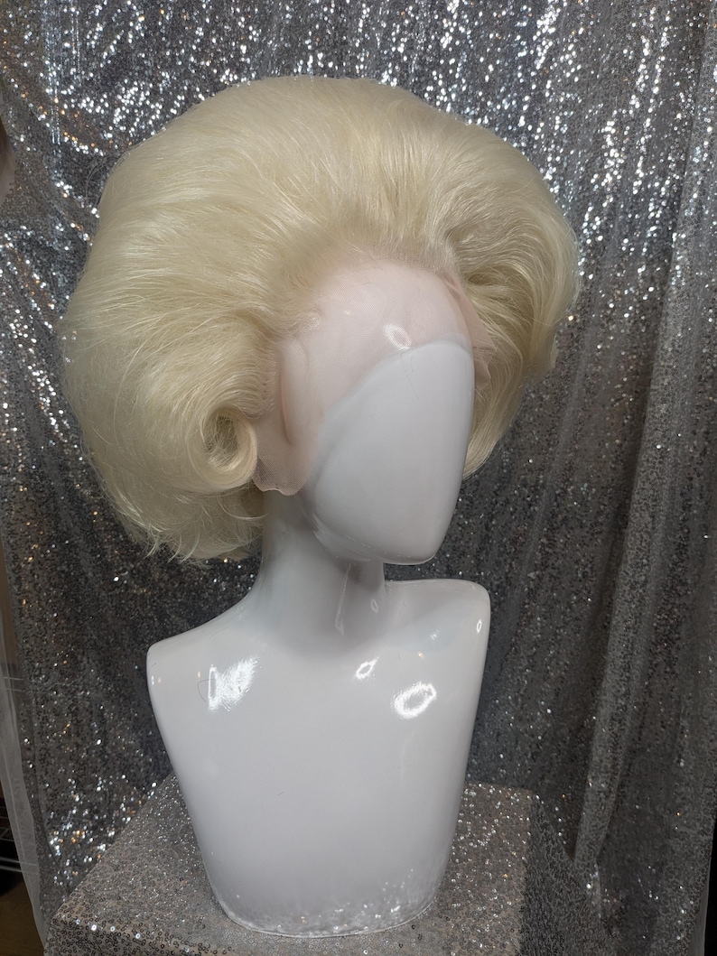 May include: A blonde wig with a bouffant style. The wig is on a white mannequin head.