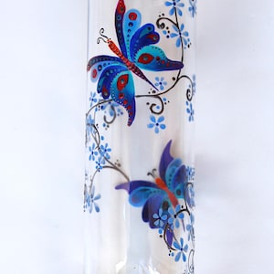 Vase streicht in der Hand, mit kleinen Schmetterlingen geschmückt, die hübsche blaue Blumen, unterschrieben und nummeriert sammeln.