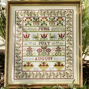Puede incluir: Un sampler de punto de cruz enmarcado con un fondo blanco y bordado colorido que representa los meses de junio, julio y agosto. El sampler presenta diseños florales, incluyendo tulipanes, bayas y hojas.