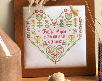 May include: A framed cross-stitch embroidery with a heart-shaped design featuring flowers, bees, and butterflies. The text reads "Polly Anne 27.08.18 8lb 10oz".
