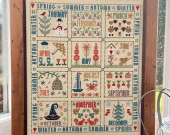 Könnte beinhalten: Ein Kreuzstich-Sampler mit einem Kalendarium, wobei jeder Monat durch eine andere Szene dargestellt wird. Die Monate sind Januar, Februar, März, April, Mai, Juni, Juli, August, September, Oktober, November und Dezember. Der Sampler ist in einem Holzrahmen gerahmt.