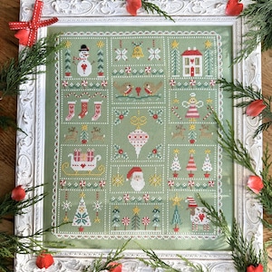 Peut inclure: Un sampler de point de croix encadré avec un fond vert et une variété d'images sur le thème de Noël, notamment un bonhomme de neige, une maison, une chaussette, un sapin de Noël et le Père Noël.
