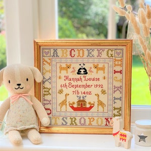May include: A framed cross-stitch with a gold frame. The cross-stitch features a colorful alphabet, animals, and the text "Hannah Louise 6th September 1992 7lb 14oz".