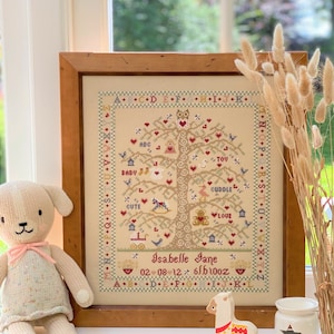 May include: A framed cross-stitch embroidery of a tree with a variety of colourful birds, animals, and words like "baby", "cute", "love", and "cuddle". The tree is surrounded by a border of letters and the name "Isabelle Jane" and the date "02 08 12 6lb10oz" are embroidered at the bottom.