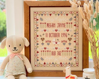 Puede incluir: Un sampler de punto de cruz enmarcado con un fondo crema y bordados coloridos. El sampler presenta el nombre "Megan Jayne", la fecha "11 de octubre de 1996" y el peso "8lb 3oz".